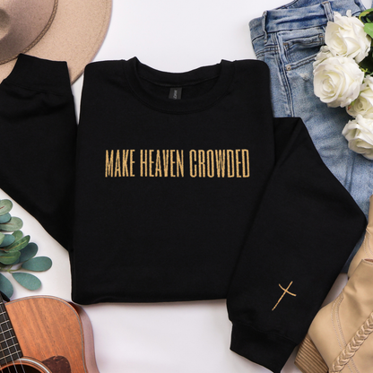 Black sweatshirt with 'MAKE HEAVEN CROWDED' text, placed on a white surface with a guitar, jeans, and flowers.