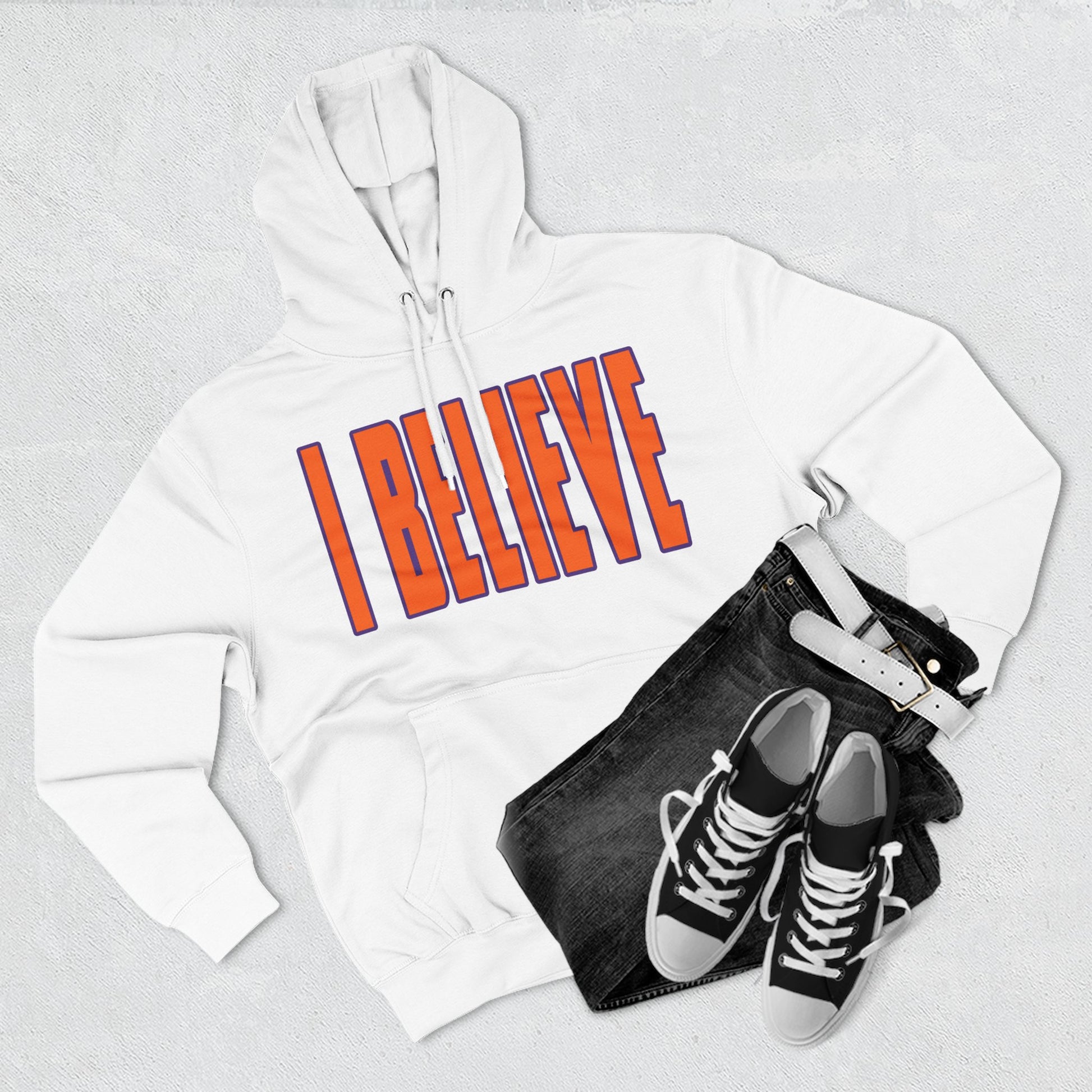 White hoodie with 'I BELIEVE' text, black jeans, and black sneakers on a light gray background