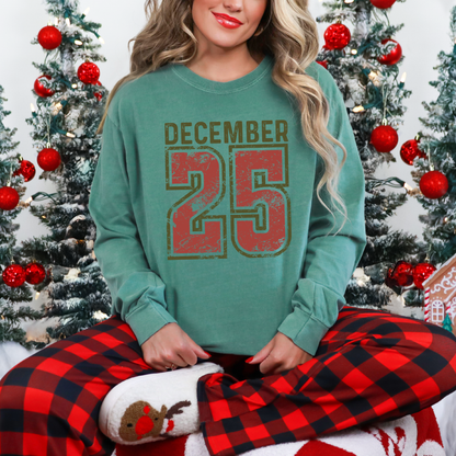 Person wearing a green sweatshirt with 'DECEMBER 25' and red plaid pants in front of Christmas trees.
