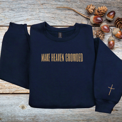 Navy blue sweatshirt with 'MAKE HEAVEN CROWDED' text on a wooden surface with autumn elements.
