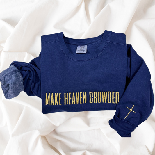 Navy blue sweatshirt with 'MAKE HEAVEN CROWDED' text and cross on a white fabric background
