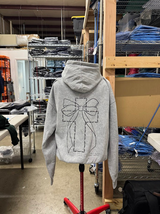 Gray hoodie with a bow design on a mannequin in a warehouse setting